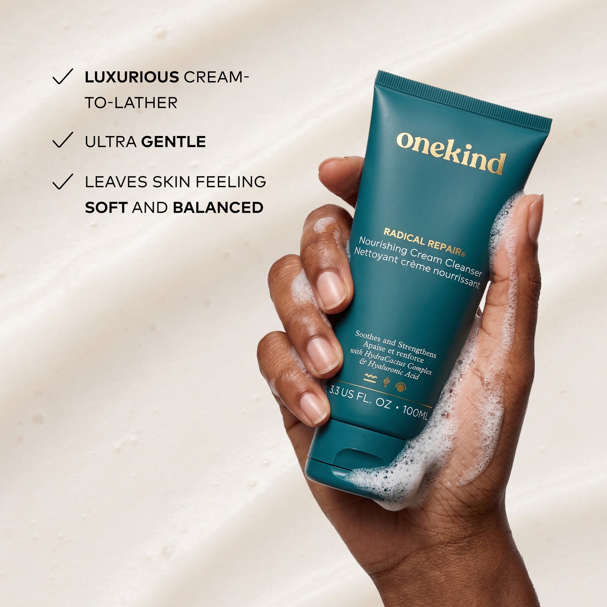 OneKind Radical Repair Nourishing Cream Cleanser being held in a hand with a light background